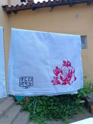 pano de prato com gravura de peônia estilizada em vermelho estampada, pendurado em um varal.