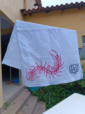 pano de prato com gravura de lacraia estilizada em vermelho estampada, pendurado em um varal.