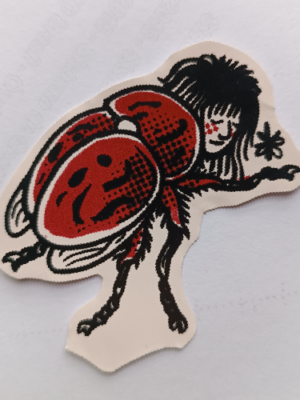 Adesivo com desenho estilizado de besouro com cabeça de mulher, em duas cores.